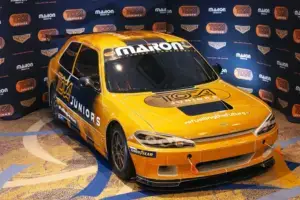 A TOCA Junior Series race car displayed indoors with a striking gold and black livery, featuring sponsor logos and "#FuellingTheFuture" branding on the hood. The car is positioned against a branded backdrop showcasing TOCA Juniors and Chevron logos.